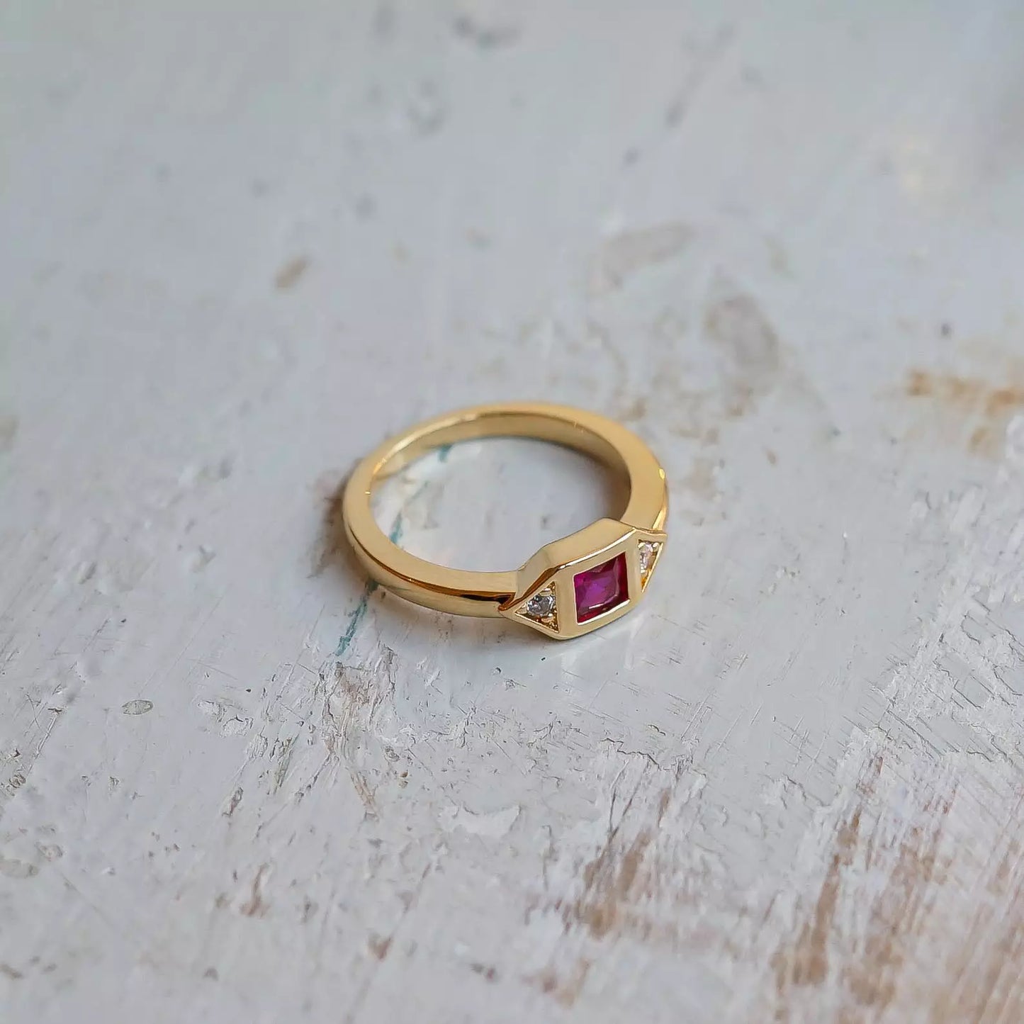 Bague femme plaquée or sertie d'une pierre de zircon couleur Fuchsia sur une table en bois