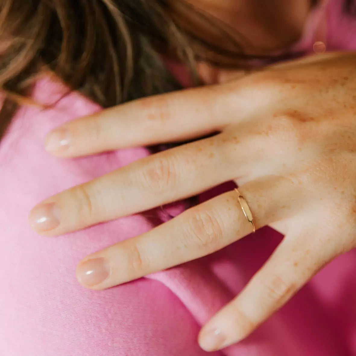 bague en or ronde identité personnalisable en gravure portée à la main par une femme avec un tee shirt rose qui touche son épaule