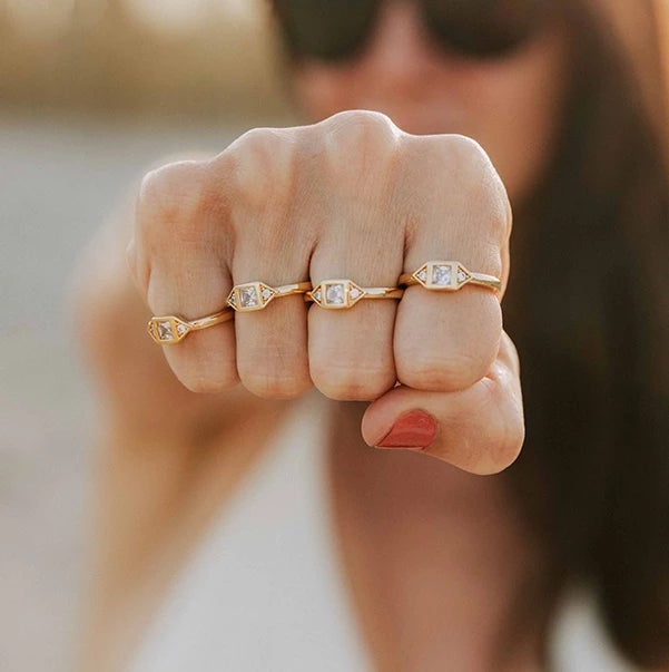 quatre bagues femme plaquées or serties de zircons couleur cristal porté sur la main d'une femme présentant son poing devant elle