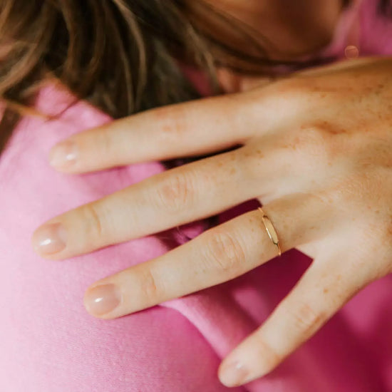 Charger l&amp;#39;image dans la galerie, bague en or ronde identité personnalisable en gravure portée à la main par une femme avec un tee shirt rose qui touche son épaule
