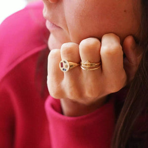 bague chevalière femme collection joie plaquée or sertie de zircons de couleurs bleus roses et cristales portée sur la main d'une femme pensive
