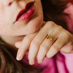 bague femme ajustable collection l'amoureuse plaquée or avec deux pierres de zircons couleur cristale qui encadrent une gravure de coeur portée par une femme qui se tient le menton