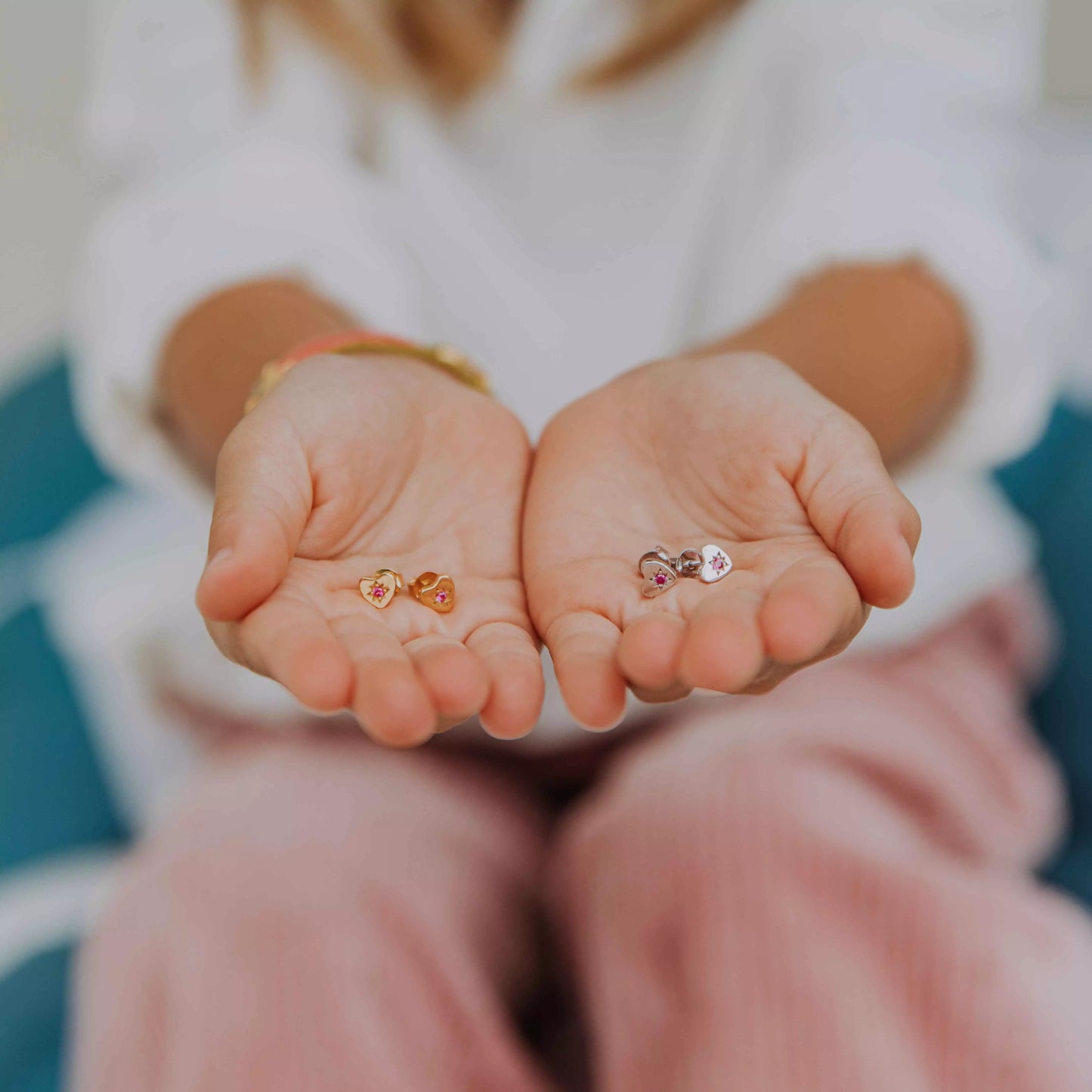 deux paires de boucles d'oreilles enfants petit coeur en argent en formes de coeur serties de zircon fuschia dans une étoile gravée présentées au creux de deux mains