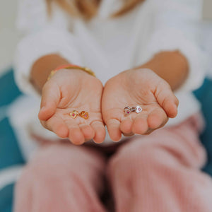 deux paires de boucles d'oreilles enfants petit coeur en vermeil en formes de coeur serties de zircon fuschia dans une étoile gravée présentées au creux de deux main
