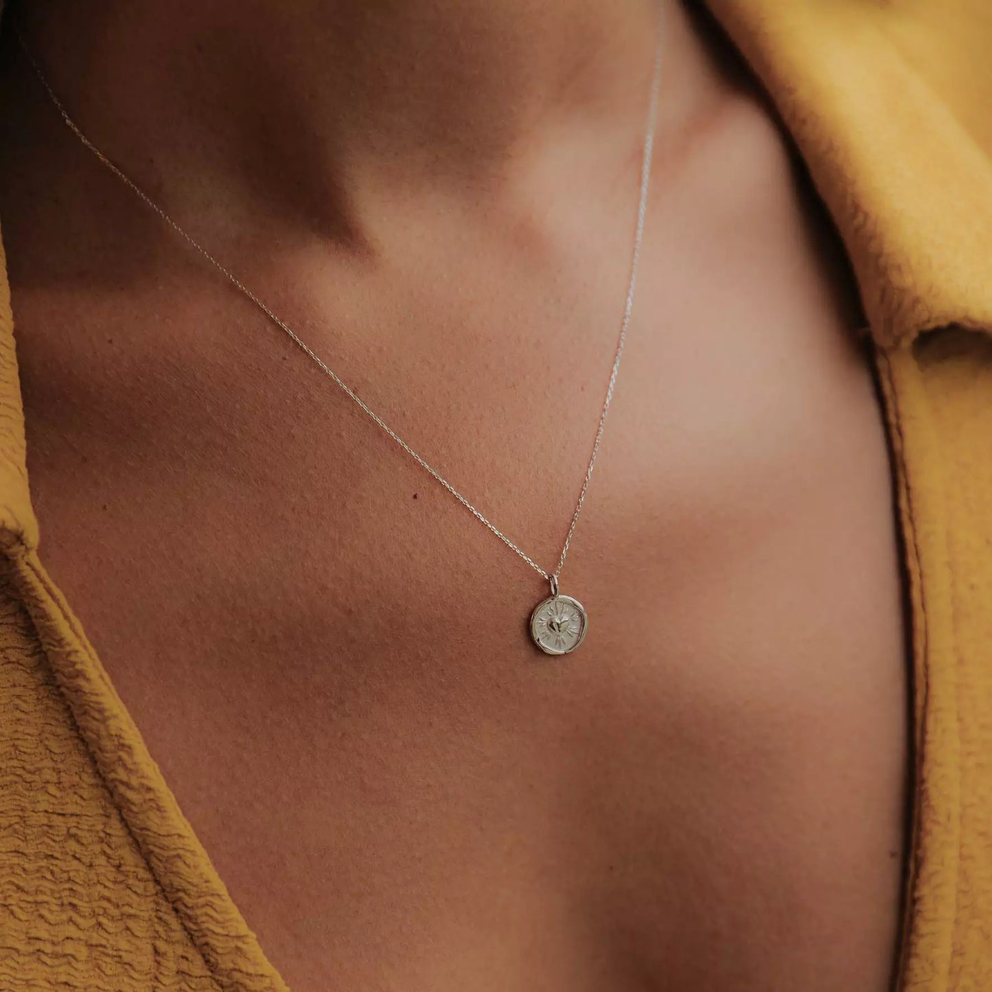 collier à gravure personnalisable pour femme collection amour en or gravé d'un coeur et de rayons porté au cou par une femme avec un haut jaune