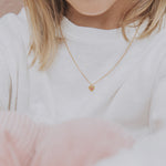 collier enfant mon petit coeur en argent en forme de coeur serti d'un zircon de couleur fuschia dans une étoile gravée porté au cou par une femme avec un haut blanc