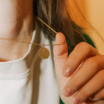 collier femme en vermeil collection solaire à gravure personnalisable de forme ronde irrégulière avec une gravure d'étoile porté au cou et reposant sur le pouce d'une femme