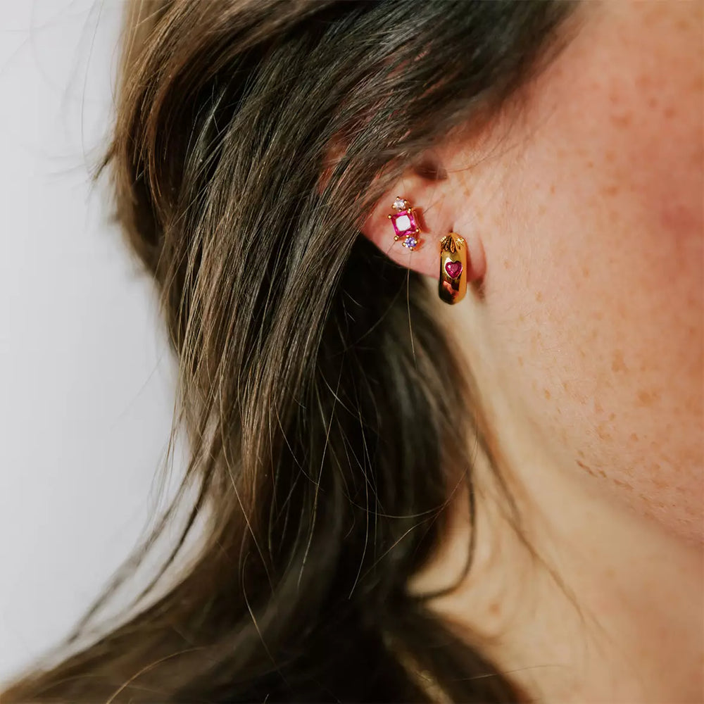 boucle d'oreille créole femme plaquée or collection l'amoureuse sertie d'un zircon couleur fuchsia en forme de coeur et gravée de rayons portée sur une oreille
