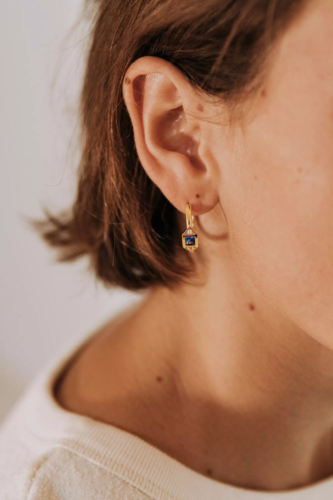 boucle d'oreille créole femme plaquée or sertie d'un zircon couleur bleu nuit et encadré de deux zircons couleur cristal portée sur une oreille