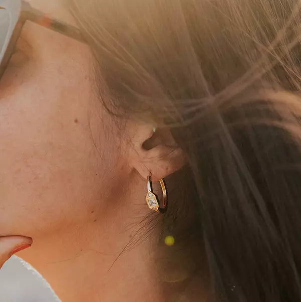 boucle d'oreille créole femme plaquée or sertie d'un zircon couleur cristal et encadré de deux zircons couleur cristal porté par une femme avec des lunettes de soleil
