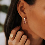 boucle d'oreille créole femme plaquée or sertie d'un zircon couleur fuchsia et encadré de deux zircons couleur cristal portée par une femme qui se touche le cou