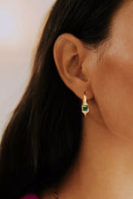 boucle d'oreille créole plaquée or sertie d'un zircon couleur vert émeraude et de deux zircons couleur cristal de chaque côté porté par une femme