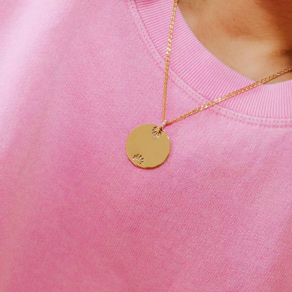 médaillon collection l'amoureuse plaqué or à gravure personnalisable avec des gravures de feuilles en haut et en bas du médaillon porté au cou par une femme avec un haut rose