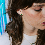 Boucle d’oreille mimi emeraude collection radieuse plaquée or serties de zircons de couleur fuchsia et emeraude portée par une femme