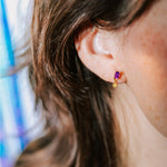 boucle d'oreille plaquée or mimi violette collection radieuse avec un serti de pierre en zircon de couleur violette et un autre serti de zircon de couleur dorée portée par une femme
