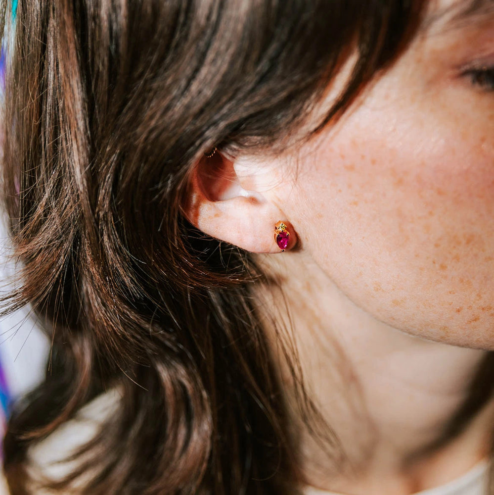 boucle d'oreille plaquée or nana rubis collection radieuse avec un serti de pierre en zircon de couleur fuchsia et un autre serti de zircon de couleur dorée portée par une femme